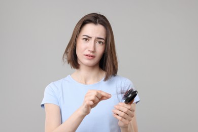 Photo of Sad woman taking her lost hair from brush on grey background. Alopecia problem