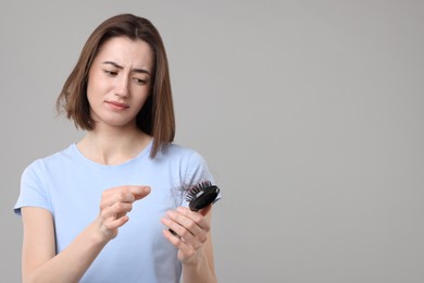 Sad woman taking her lost hair from brush on grey background, space for text. Alopecia problem