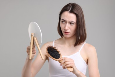 Sad woman with hair loss problem looking at mirror on grey background