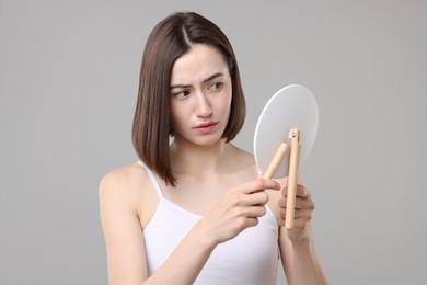 Photo of Sad woman with hair loss problem looking at mirror on grey background