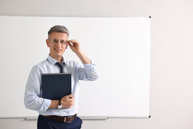 Photo of Teacher with notebook near whiteboard in classroom
