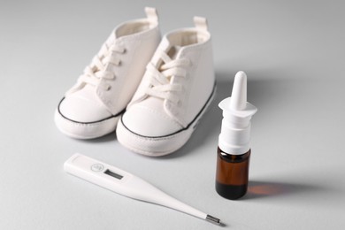 Photo of Child`s sneakers, thermometer and nasal spray on grey table, closeup
