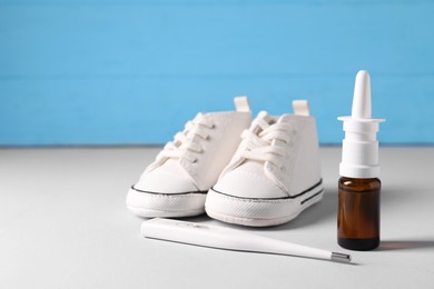 Child`s sneakers, thermometer and nasal spray on grey table, closeup