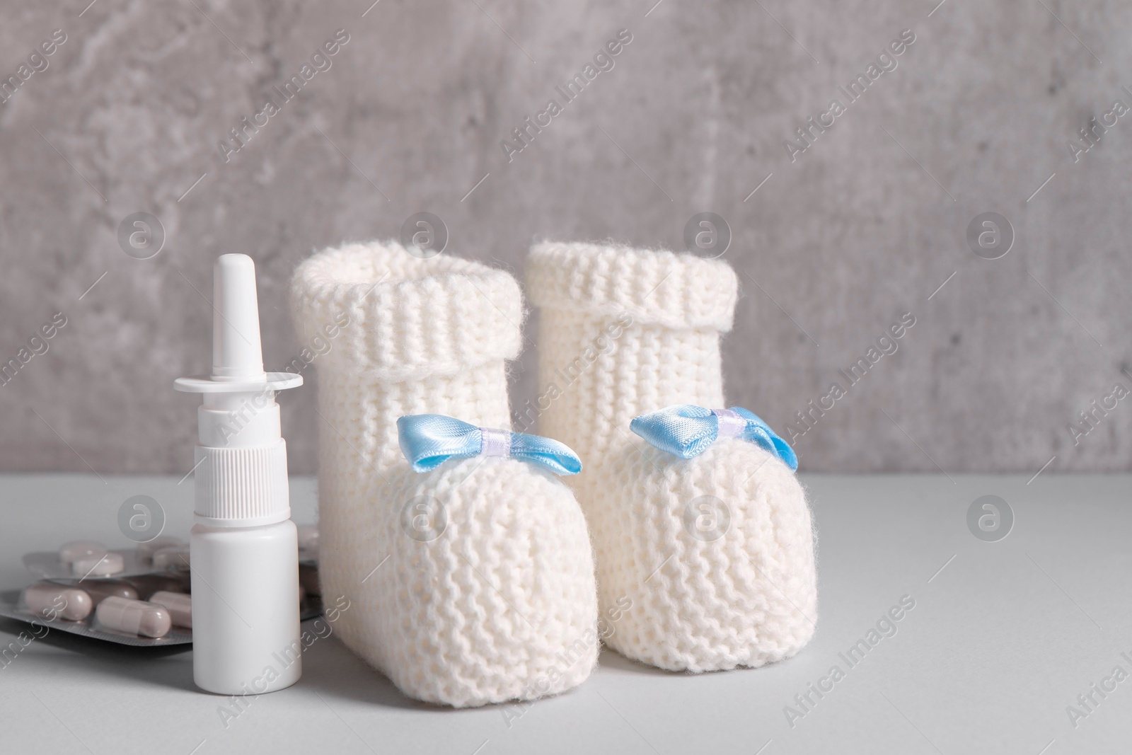 Photo of Baby`s booties, nasal spray and pills on grey table, closeup