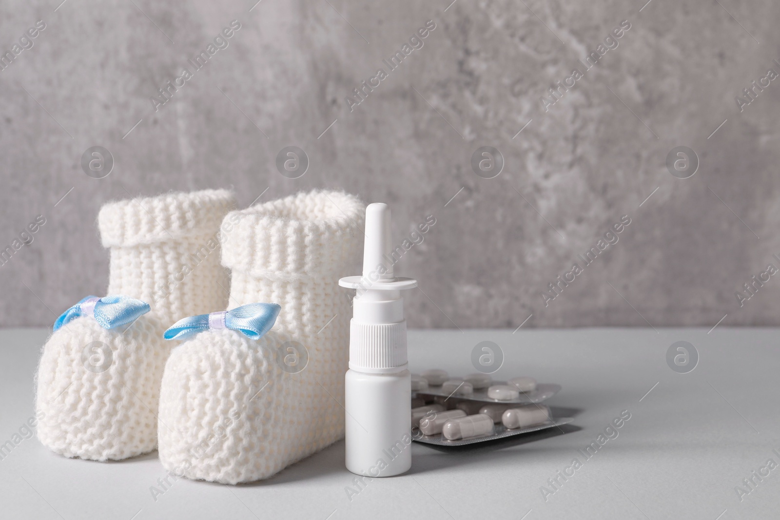 Photo of Baby`s booties, nasal spray and pills on grey table, closeup