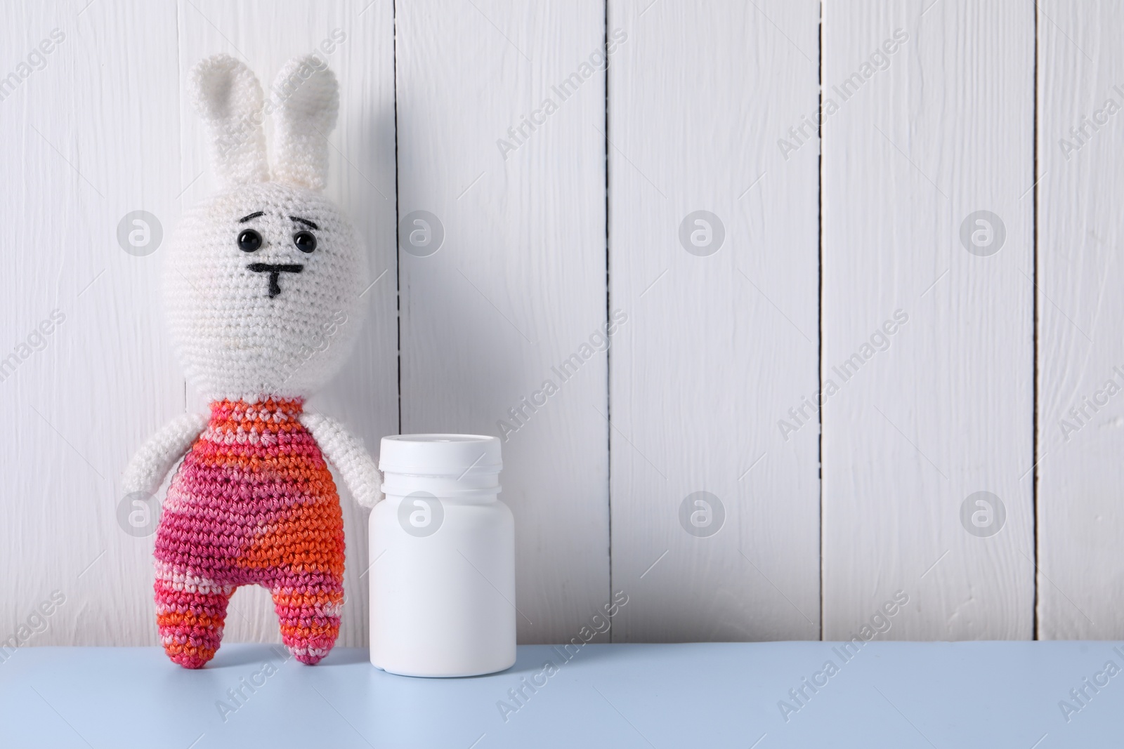 Photo of Toy bunny and bottle of pills on light blue table near white wooden wall, space for text