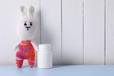 Toy bunny and bottle of pills on light blue table near white wooden wall, space for text