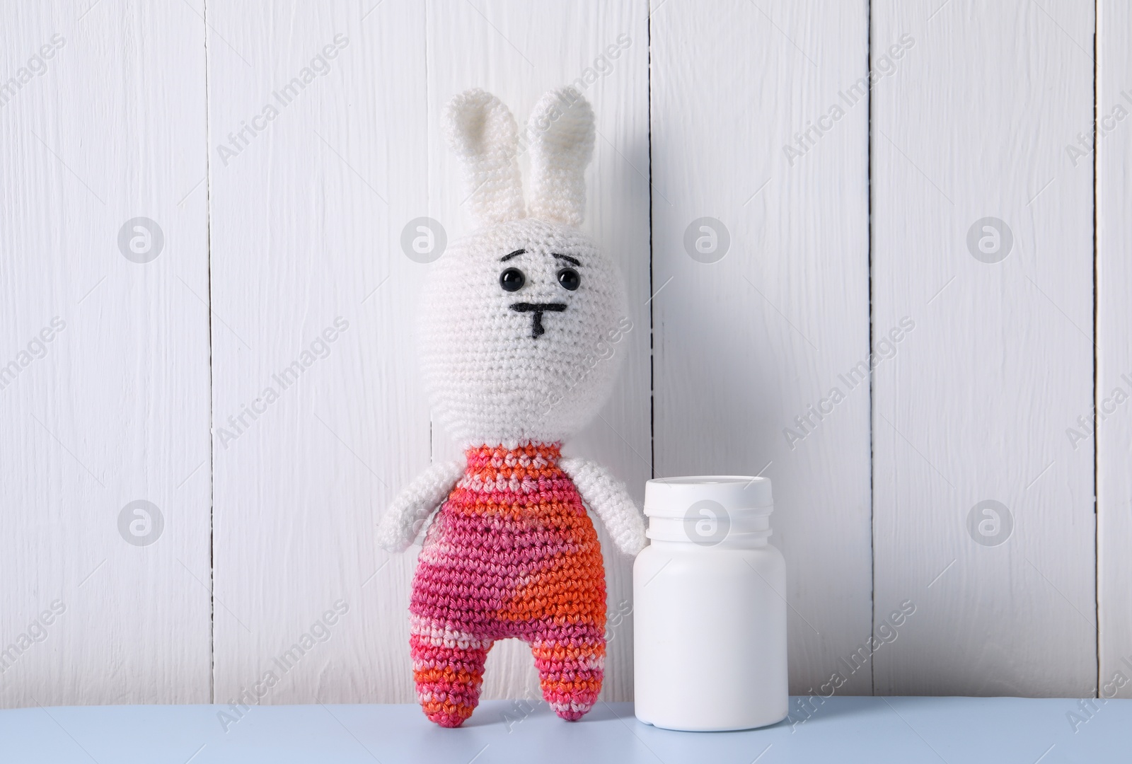 Photo of Toy bunny and bottle of pills on light blue table near white wooden wall