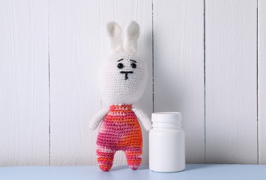 Photo of Toy bunny and bottle of pills on light blue table near white wooden wall