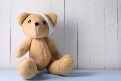 Photo of Toy bear with bandage on light blue table near white wooden wall, space for text