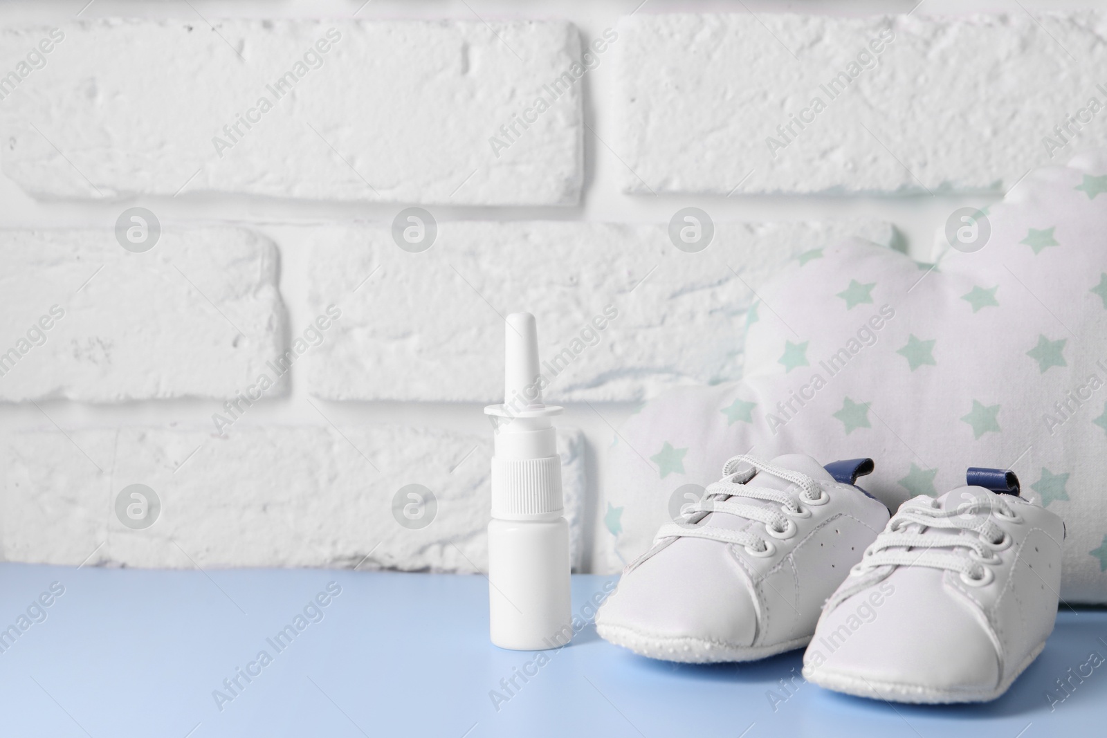 Photo of Nasal spray, child`s sneakers and cloud shaped pillow on light blue table near white brick wall, space for text