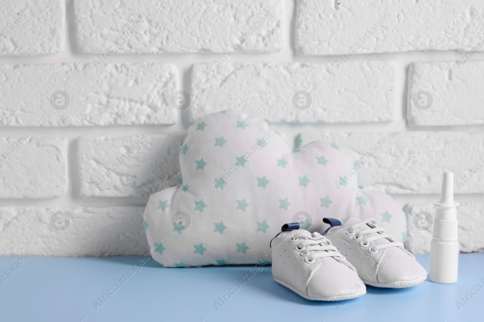 Photo of Nasal spray, child`s sneakers and cloud shaped pillow on light blue table near white brick wall