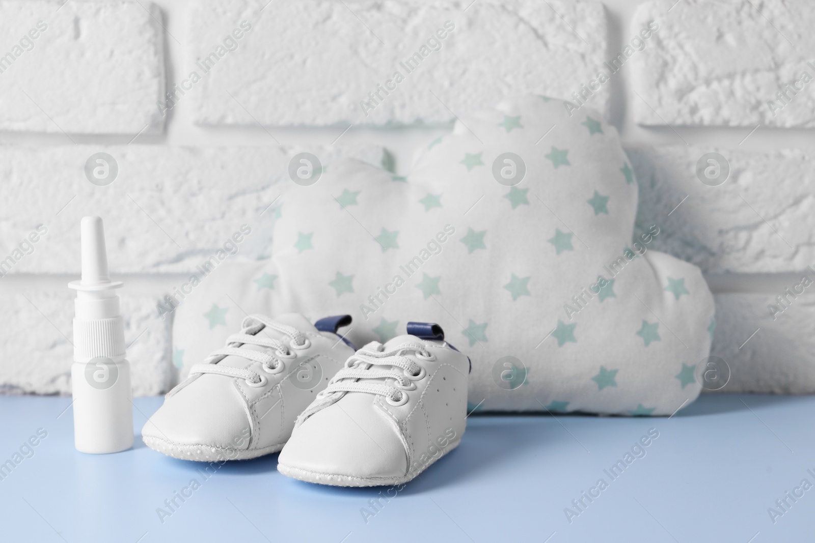 Photo of Nasal spray, child`s sneakers and cloud shaped pillow on light blue table near white brick wall