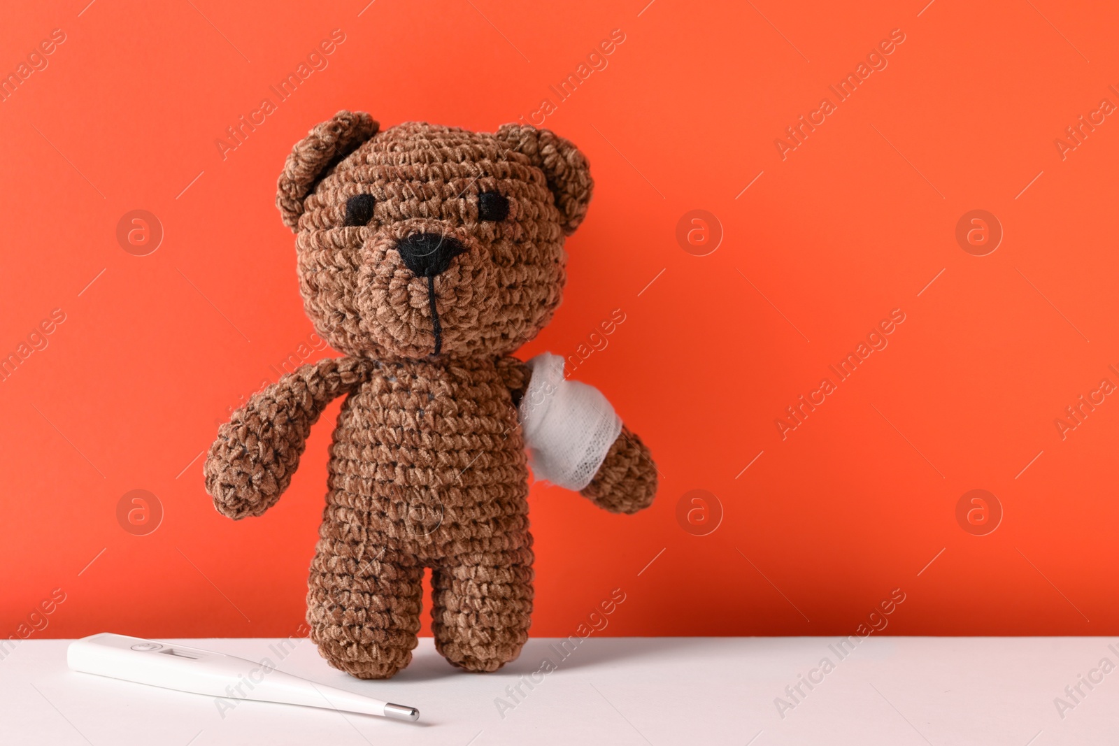 Photo of Toy bear with bandage and thermometer on color background, space for text