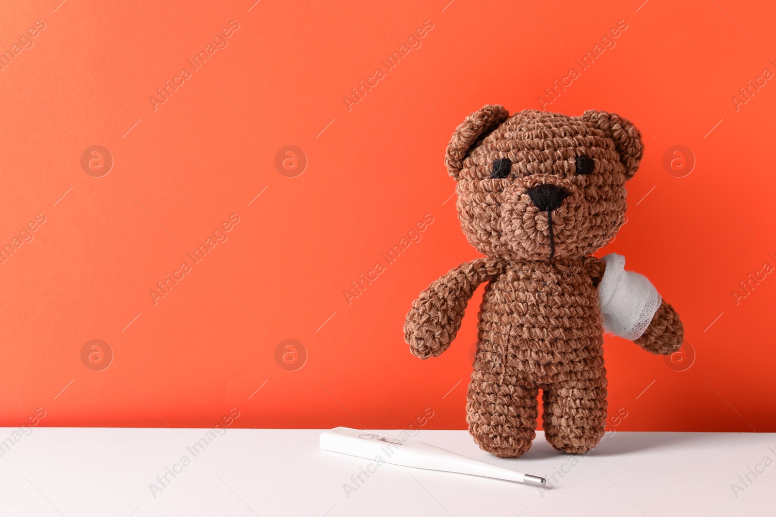 Photo of Toy bear with bandage and thermometer on color background, space for text