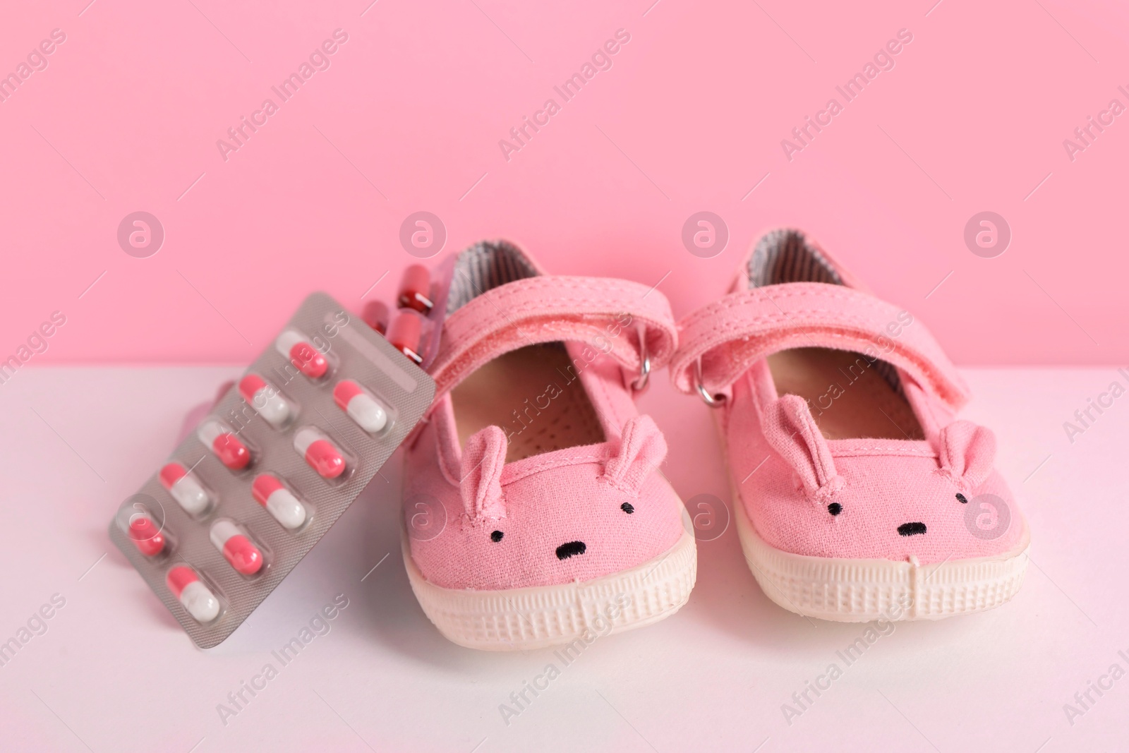 Photo of Cute baby shoes and pills on color background