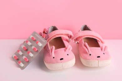 Cute baby shoes and pills on color background