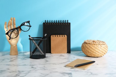 Photo of Stylish office workplace. Decor elements, glasses and stationery on white table near light blue wall