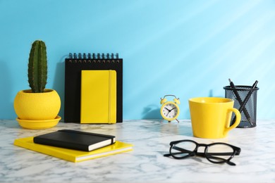 Photo of Stylish office workplace. Decor elements, glasses, cup and stationery on marble table near light blue wall