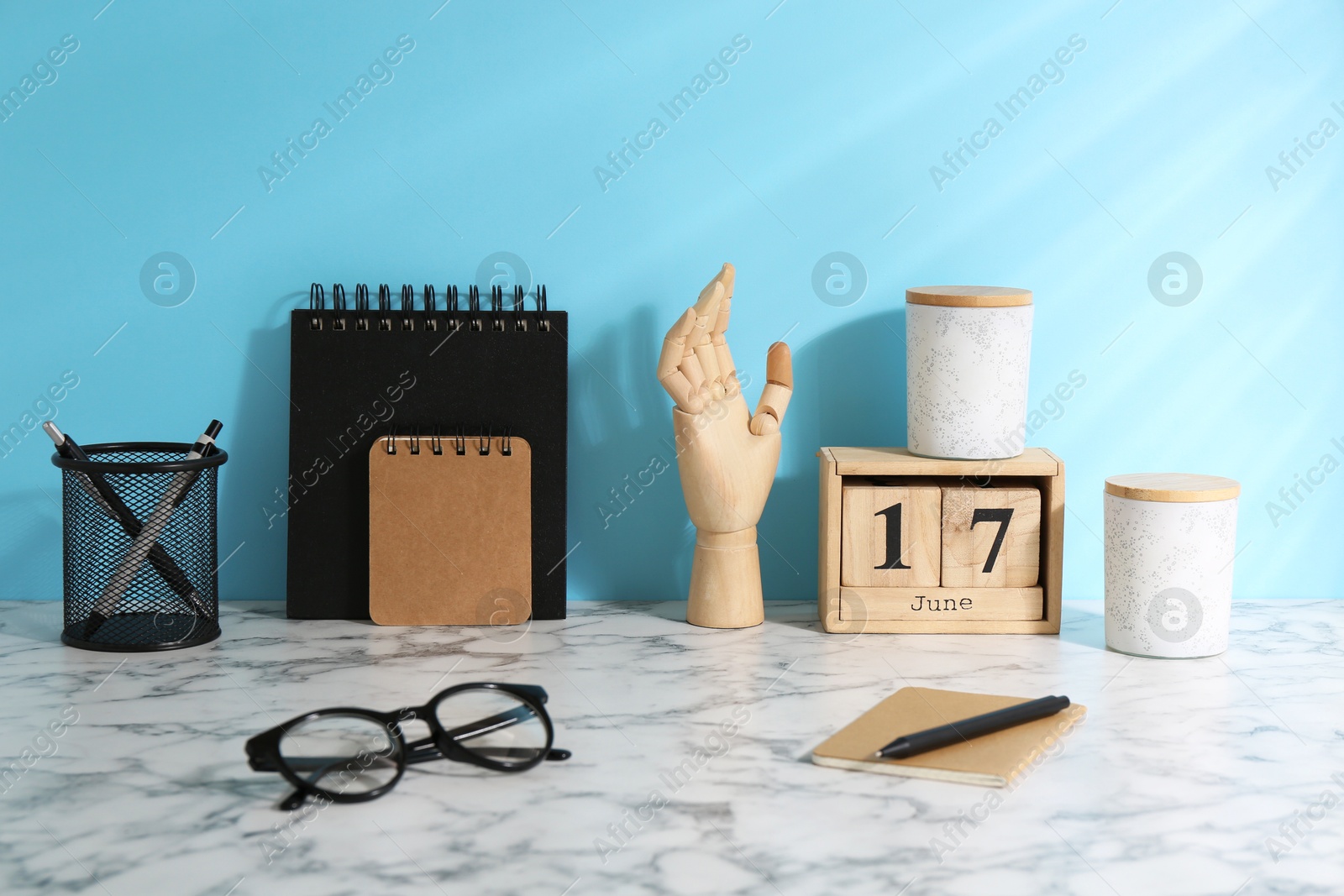 Photo of Stylish office workplace. Decor elements, glasses and stationery on white table near light blue wall