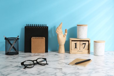 Photo of Stylish office workplace. Decor elements, glasses and stationery on white table near light blue wall