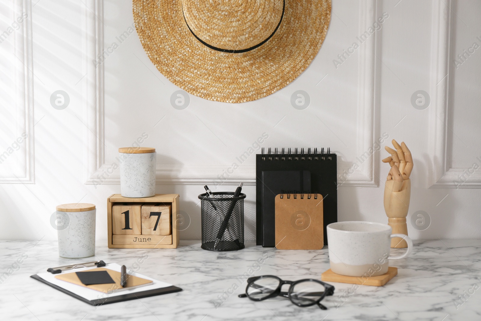 Photo of Stylish office workplace. Decor elements, glasses, cup and stationery on marble table near white wall