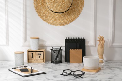 Photo of Stylish office workplace. Decor elements, glasses, cup and stationery on marble table near white wall