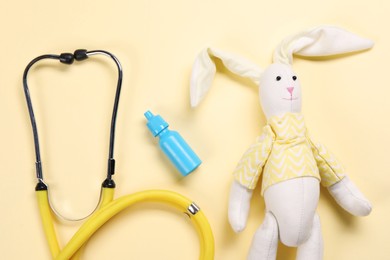 Photo of Toy bunny, stethoscope and nasal spray on yellow background, flat lay