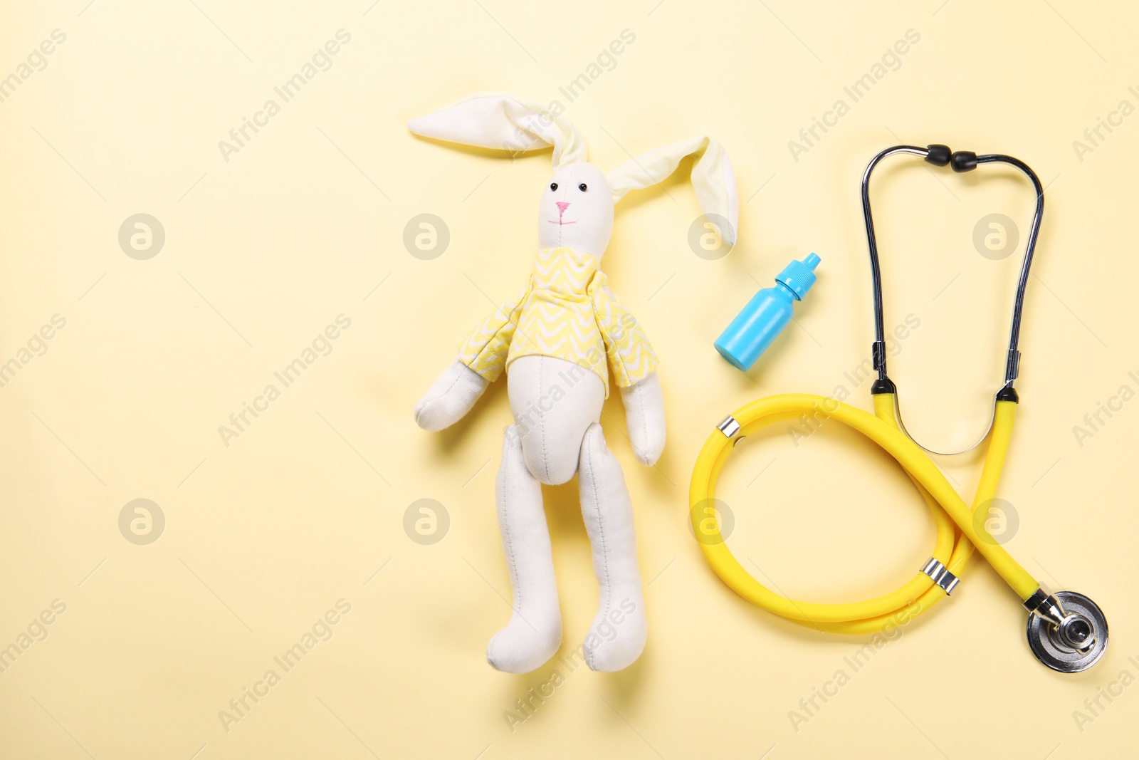 Photo of Toy bunny, stethoscope and nasal spray on yellow background, flat lay. Space for text