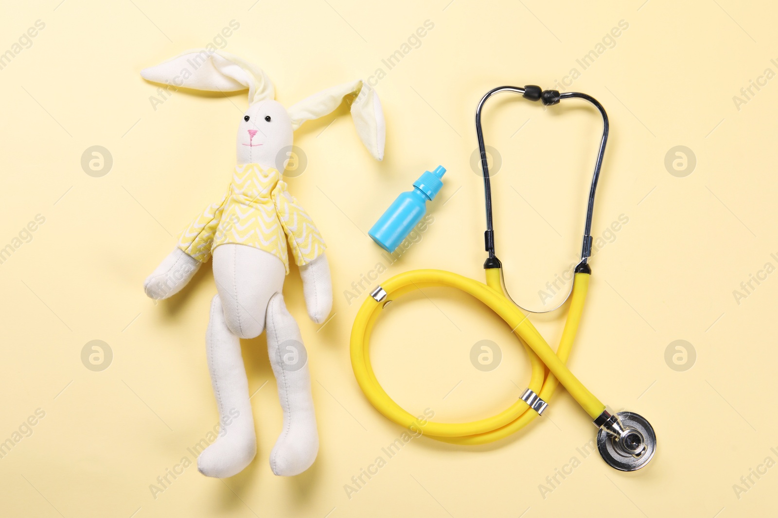 Photo of Toy bunny, stethoscope and nasal spray on yellow background, flat lay