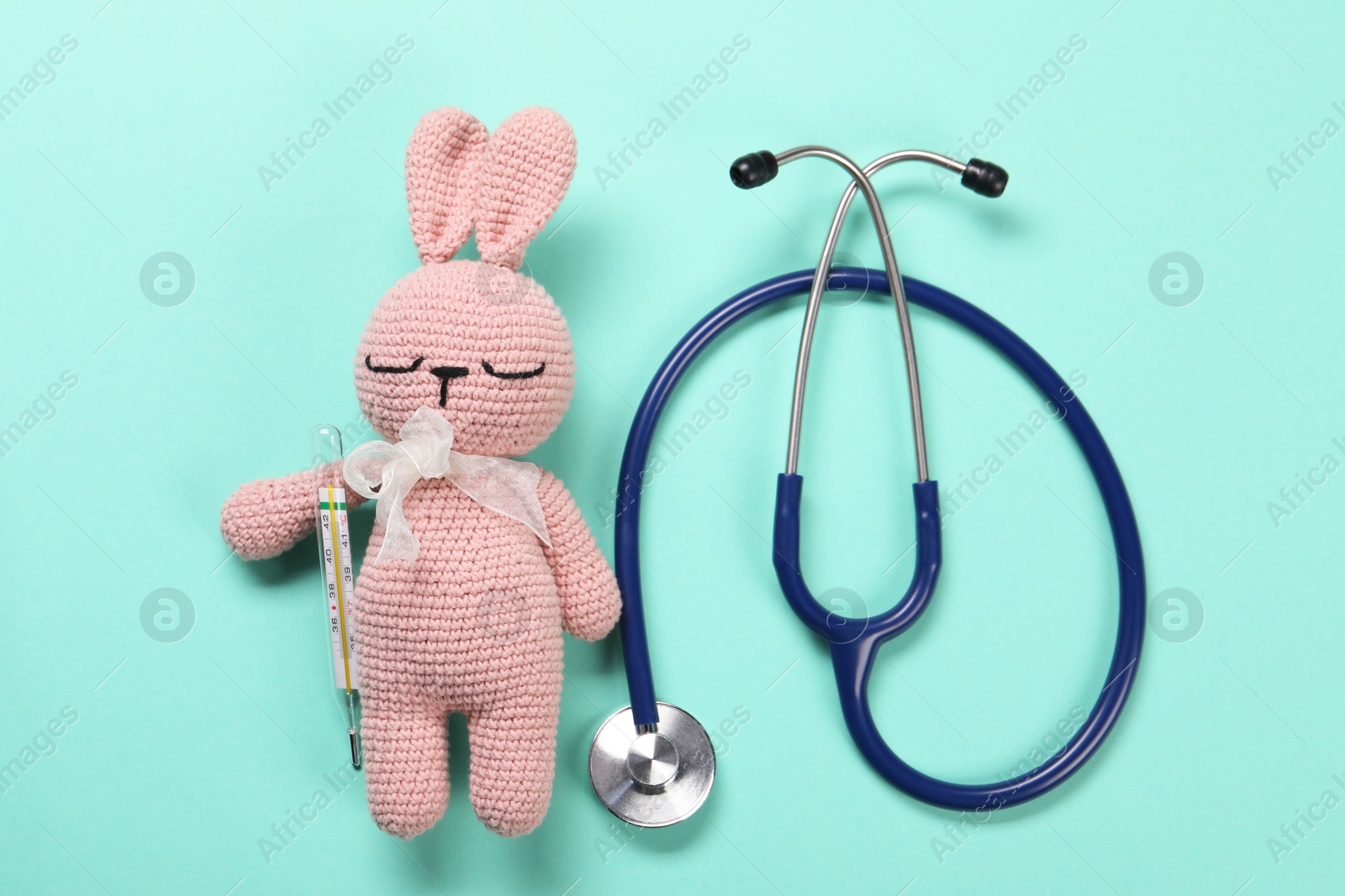 Photo of Toy bunny, stethoscope and thermometer on turquoise background, flat lay