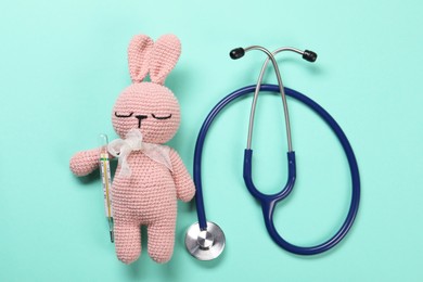 Photo of Toy bunny, stethoscope and thermometer on turquoise background, flat lay