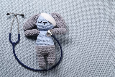 Photo of Toy bunny and stethoscope on gray blanket, top view. Space for text