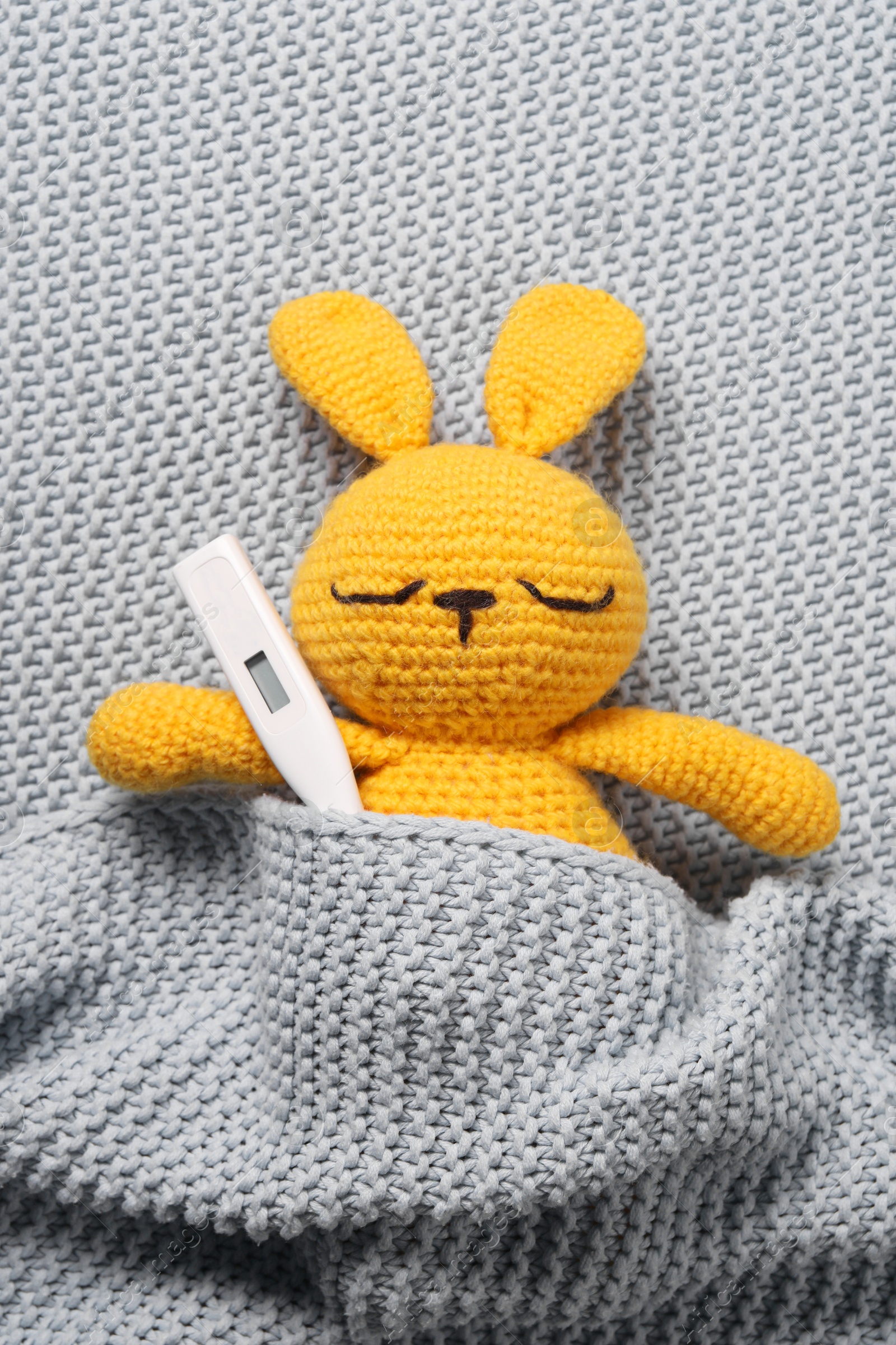 Photo of Toy bunny with thermometer under blanket, top view