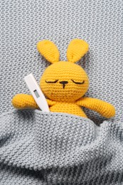 Photo of Toy bunny with thermometer under blanket, top view