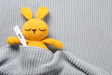 Toy bunny with thermometer under blanket, top view. Space for text