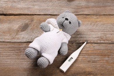 Photo of Toy bear and thermometer on wooden background, above view