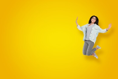 Image of Positive young woman jumping on yellow gradient background. Space for text