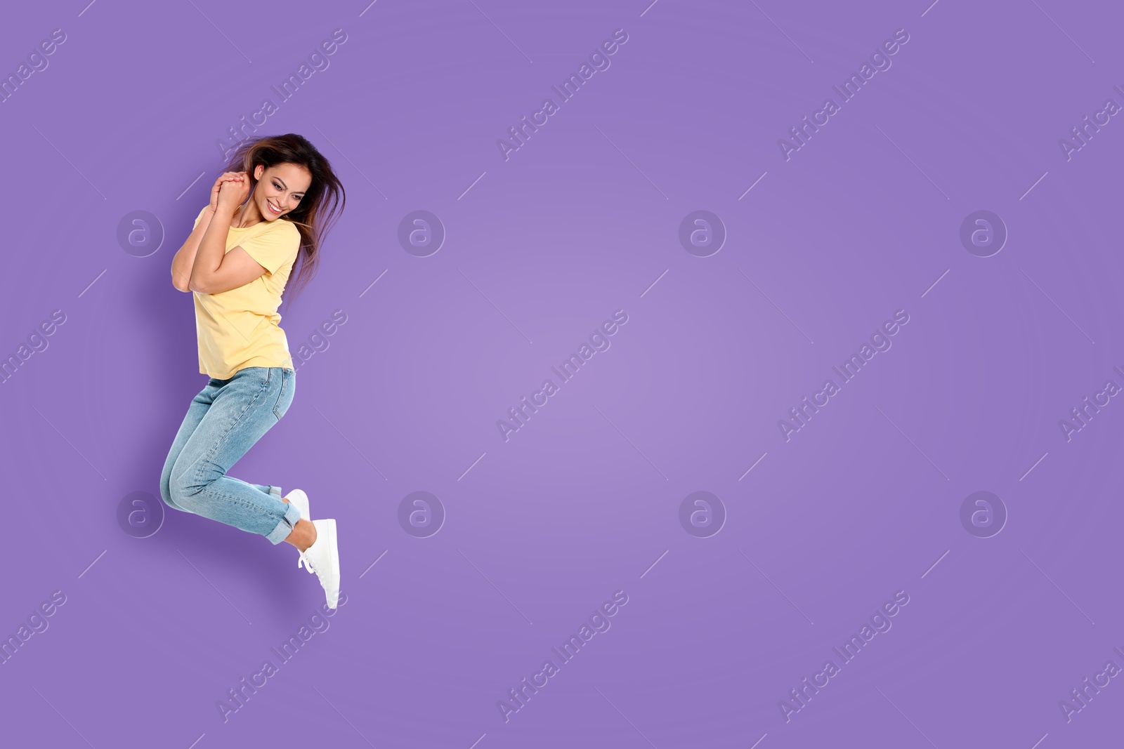 Image of Positive young woman jumping on purple background. Space for text