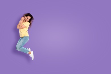 Positive young woman jumping on purple background. Space for text