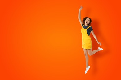 Image of Positive young woman jumping on dark orange background. Space for text