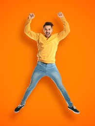 Positive young man jumping on orange background
