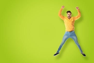 Positive young man jumping on light green background. Space for text