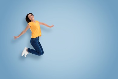 Positive young woman jumping on light blue background. Space for text