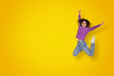 Image of Positive young woman jumping on yellow background. Space for text