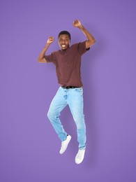 Positive young man jumping on purple background