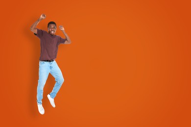 Positive young man jumping on dark orange background. Space for text
