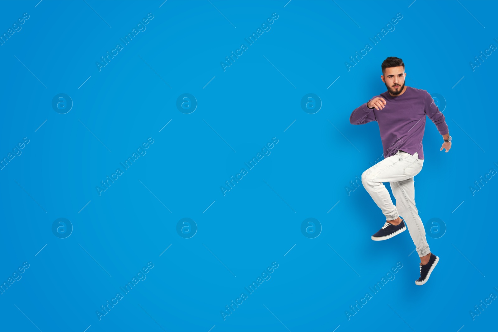 Image of Positive young man jumping on blue background. Space for text