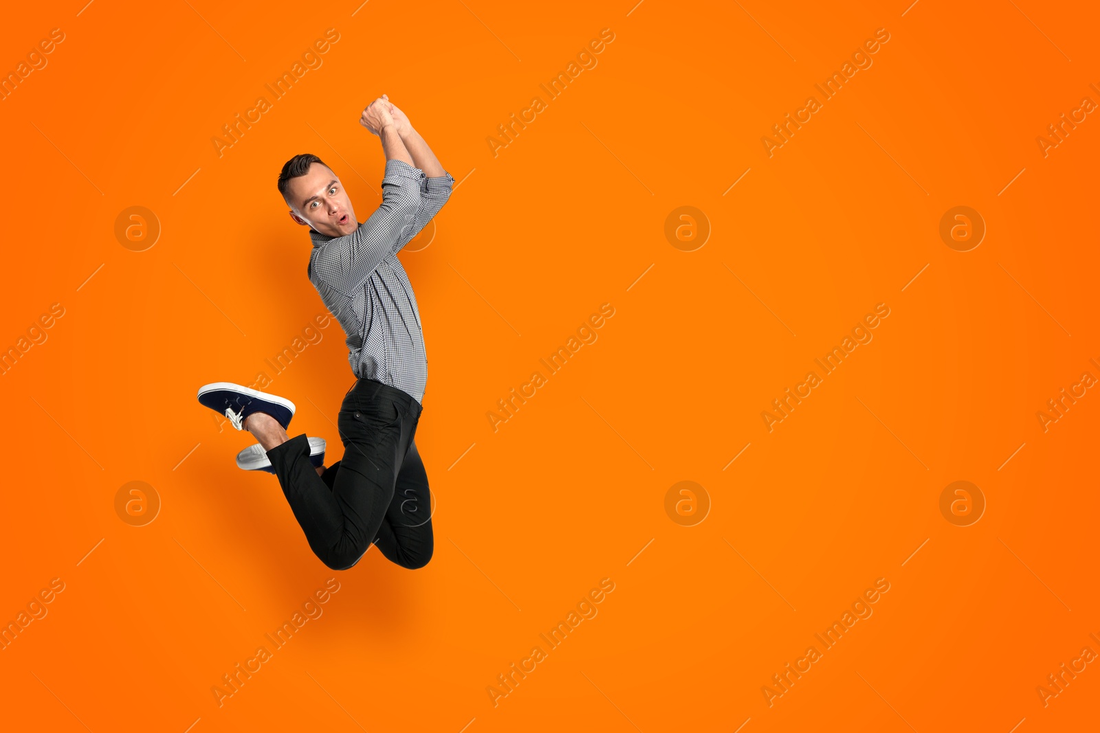 Image of Positive young man jumping on orange background. Space for text
