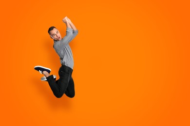 Image of Positive young man jumping on orange background. Space for text